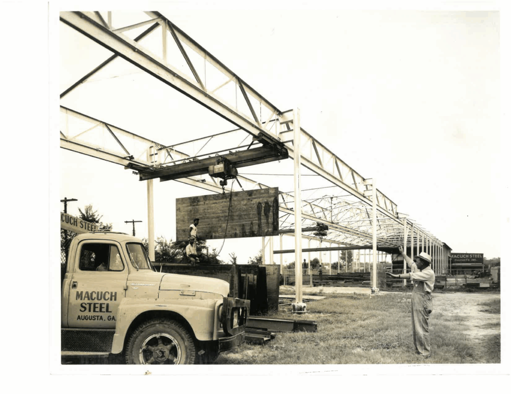 Macuch Steel team installing structural steel beams at a construction site in the 1950s. An old truck with the Macuch Steel name is visible onsite.
